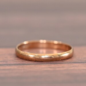 May include: A gold-colored ring with a smooth, rounded design. The ring is set against a wooden surface, showcasing its polished finish. This piece of jewelry is a classic and timeless accessory.