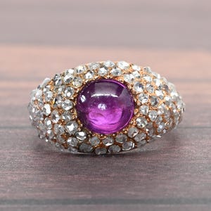 May include: A ring with a large, round, purple gemstone surrounded by smaller, white gemstones.