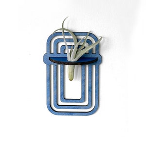 May include: A blue wooden wall planter with a geometric design. The planter has a small shelf for holding a small air plant.