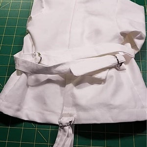 May include: White cotton jacket with a long, white sash tied at the waist. The sash has two silver rings on each side.