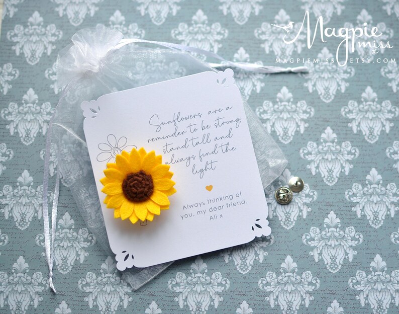 May include: A yellow felt sunflower attached to a white card with a decorative edge. The card has text that reads "Sunflowers are a reminder to be strong, stand tall and always find the light." The card is in a sheer bag.