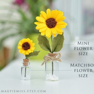 K&ouml;nnte beinhalten: Zwei Filz-Sonnenblumen in Glasflaschen. Die gr&ouml;&szlig;ere Sonnenblume ist mit "Matchbox Flower Size" und die kleinere Sonnenblume mit "Mini Flower Size" beschriftet.