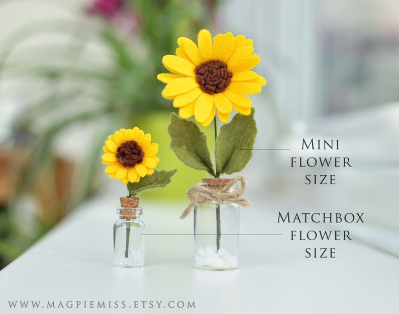 K&ouml;nnte beinhalten: Zwei Filz-Sonnenblumen in Glasflaschen. Die gr&ouml;&szlig;ere Sonnenblume ist mit "Matchbox Flower Size" und die kleinere Sonnenblume mit "Mini Flower Size" beschriftet.