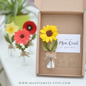 May include: A small, brown cardboard box with a felt sunflower in a glass bottle. The sunflower is yellow with a brown center. The box has a white card that says "Add a Mini Card to your box!"