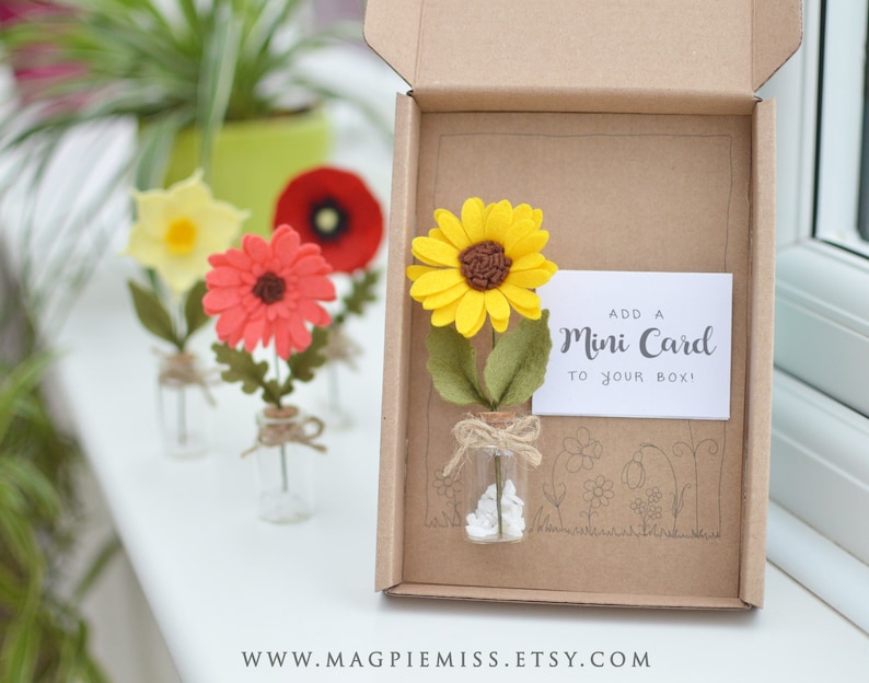 May include: A small, brown cardboard box with a felt sunflower in a glass bottle. The sunflower is yellow with a brown center. The box has a white card that says "Add a Mini Card to your box!"