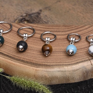 May include: Five earrings with silver hoops and gemstone beads in various colors: dark green, black, brown, light blue, and white with gray marbling. The earrings are displayed on a wooden surface.