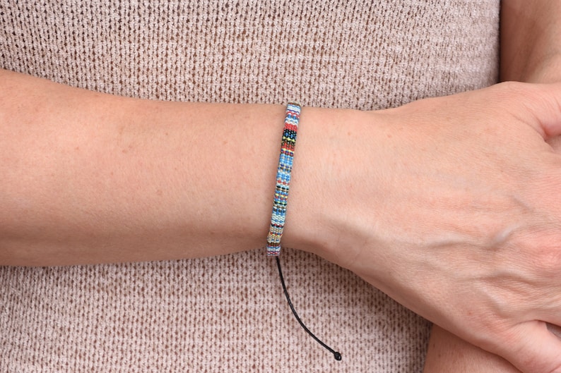 Peut inclure: Un bracelet en perles color&eacute;es avec un cordon noir. Le bracelet pr&eacute;sente une vari&eacute;t&eacute; de couleurs, notamment le bleu, le rouge, le blanc et le noir.