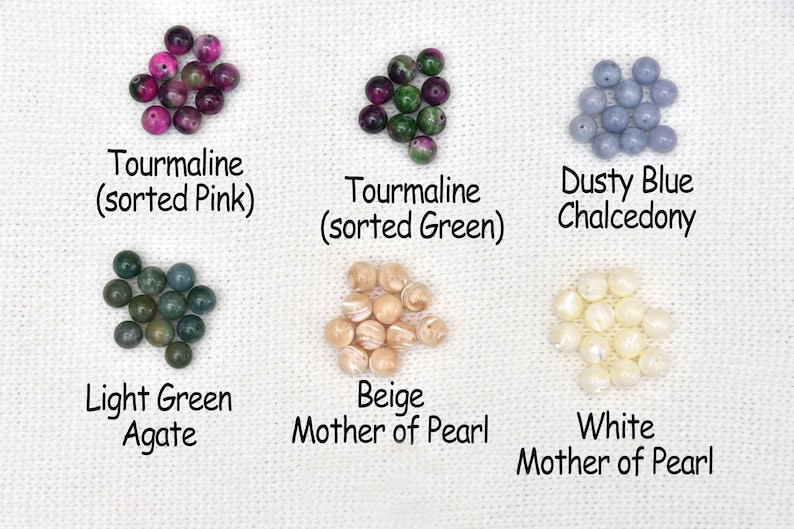 May include: An assortment of gemstone beads in various colors, including pink and green tourmaline, dusty blue chalcedony, light green agate, and beige and white mother of pearl. Text labels identify each type of bead.
