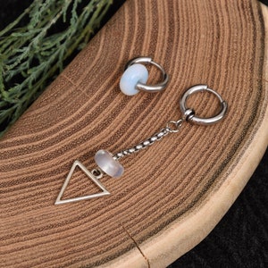Puede incluir: Dos pendientes de plata con una piedra blanca. Un pendiente es un aro y el otro es un triángulo con una cadena y una piedra blanca.