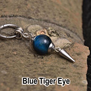 May include: A single earring featuring a blue tiger eye bead and a silver-coloured cone charm. The earring is attached to a silver-coloured hoop. The text "Blue Tiger Eye" is displayed below the earring.