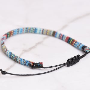 Peut inclure: Un bracelet tiss&eacute; color&eacute; avec un cordon noir et une fermeture &agrave; n&oelig;ud r&eacute;glable.