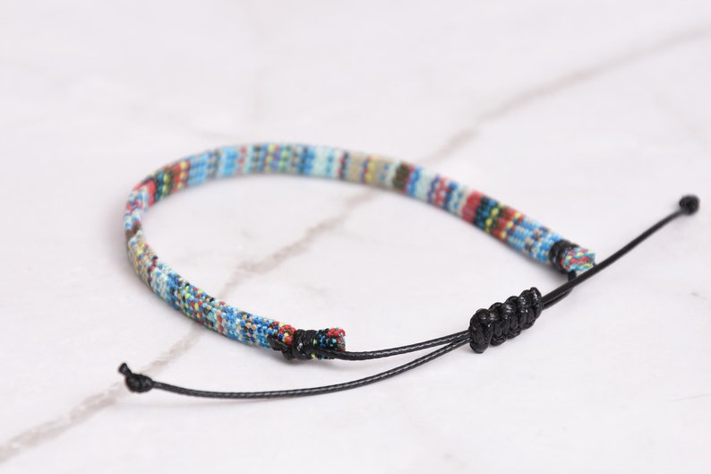 Peut inclure: Un bracelet tiss&eacute; color&eacute; avec un cordon noir et une fermeture &agrave; n&oelig;ud r&eacute;glable.