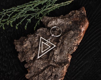 May include: Silver double triangle pendant with a silver ring attached to a chain. The pendant is on a piece of tree bark.