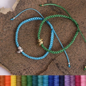May include: Two friendship bracelets with a silver and gold charm. The bracelets are made with blue and green cord. The cord is available in a variety of colors.