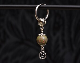 May include: A silver hoop earring with a dangling pendant. The pendant features a green and red stone bead, a decorative silver bead, and a silver spiral charm. The earring is suspended against a dark background.