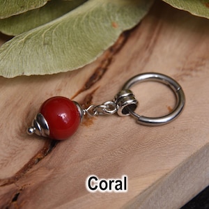 May include: A single earring with a red coral bead and a silver-colored hoop. The coral bead has a shiny finish and a silver-colored conical cap. The word "Coral" is written in white text at the bottom of the image.