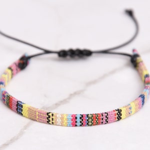 Peut inclure: Un bracelet tiss&eacute; color&eacute; avec un cordon noir r&eacute;glable. Le bracelet pr&eacute;sente une vari&eacute;t&eacute; de couleurs, notamment le rose, le jaune, le bleu et le vert.