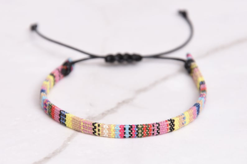 Peut inclure: Un bracelet tiss&eacute; color&eacute; avec un cordon noir r&eacute;glable. Le bracelet pr&eacute;sente une vari&eacute;t&eacute; de couleurs, notamment le rose, le jaune, le bleu et le vert.