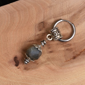 Puede incluir: Un solo pendiente de plata con un colgante de piedra preciosa gris facetada. El pendiente presenta una cuenta decorativa de plata y un aro de plata. El pendiente se muestra sobre una superficie de madera.