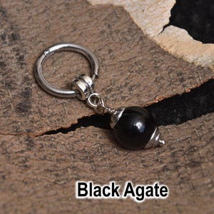 May include: A silver-colored hoop earring with a black agate bead pendant. The bead is a glossy black with silver-colored metal accents. The text "Black Agate" is at the bottom of the image.