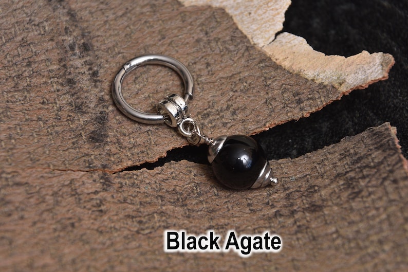May include: A silver-colored hoop earring with a black agate bead pendant. The bead is a glossy black with silver-colored metal accents. The text "Black Agate" is at the bottom of the image.