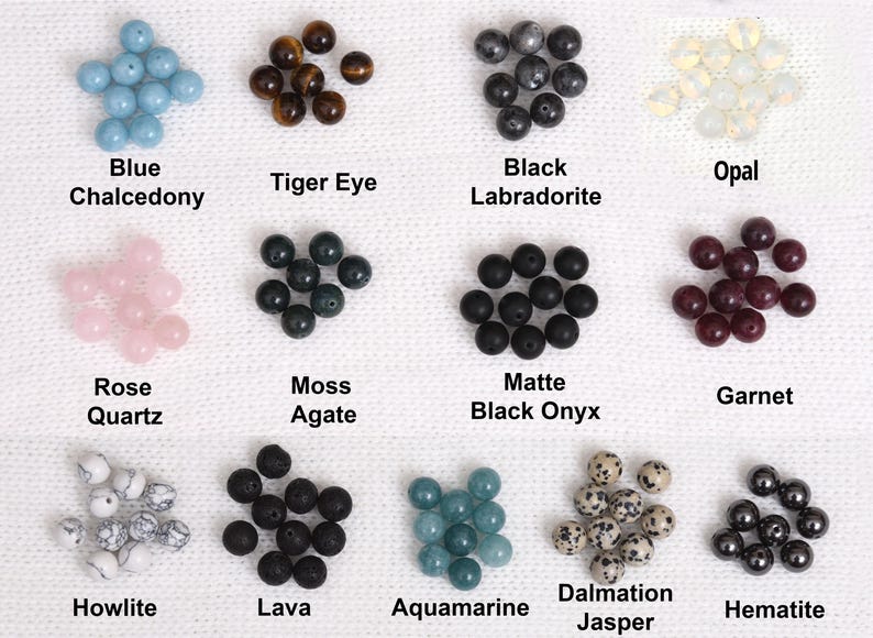 May include: A collection of gemstone beads in various colors and types, including blue chalcedony, tiger eye, black labradorite, and opal. Other stones include rose quartz, moss agate, matte black onyx, and garnet. Additional beads are howlite, lava, aquamarine, dalmatian jasper, and hematite.