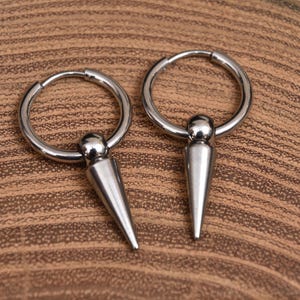 Puede incluir: Un par de pendientes de aro de plata con una punta puntiaguda que cuelga de cada aro.