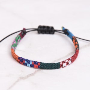 Peut inclure: Un bracelet tiss&eacute; color&eacute; avec une fermeture en cordon noir r&eacute;glable. Le bracelet pr&eacute;sente une vari&eacute;t&eacute; de couleurs, notamment le rouge, l'orange, le jaune, le vert, le bleu et le violet.