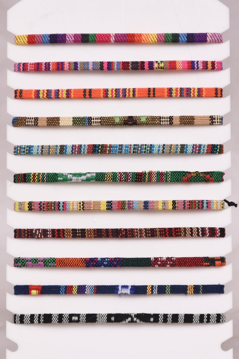 Peut inclure: Une vari&eacute;t&eacute; de cordons tiss&eacute;s color&eacute;s, pr&eacute;sent&eacute;s sur une carte blanche, chaque cordon pr&eacute;sentant un motif unique.