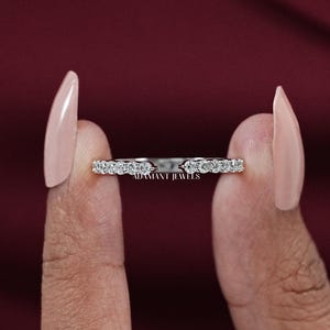 May include: A silver-toned ring featuring a row of small, clear, round-cut stones set along the band. The ring has a distinct open gap design at the center. The text ADAMANT JEWELS is clearly visible in small print on the inner surface of the band.
