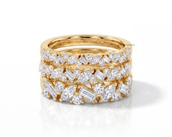 May include: A stack of three yellow gold rings, each featuring a cluster of clear, faceted stones in various shapes, including round, marquise, and baguette cuts. The rings are arranged vertically, showcasing a dense, sparkling arrangement of gems.