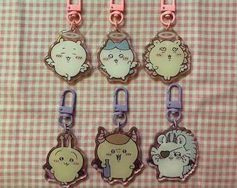 May include: Six acrylic keychains with cartoon animal designs. Each keychain features a different character with a unique expression and details, such as angel wings or devil horns. The keychains have pink and purple clasps.
