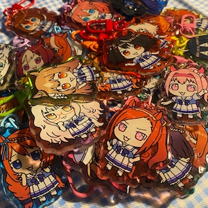 May include: A collection of colorful anime-style character keychains. The keychains feature various characters with different hair colors and outfits. Each keychain has a metal clasp for attachment.