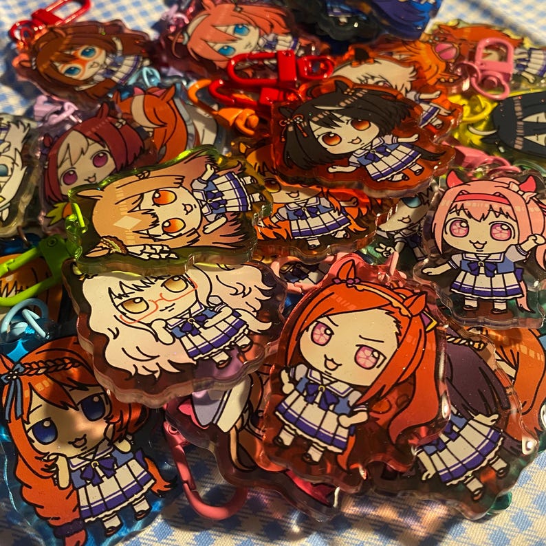 May include: A collection of colorful anime-style character keychains. The keychains feature various characters with different hair colors and outfits. Each keychain has a metal clasp for attachment.