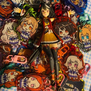 May include: A collection of anime-style keychains and a figurine. The keychains feature various cartoon characters with large eyes and colorful outfits. The figurine is of a character in a yellow and red outfit. The keychains have various colored clasps.