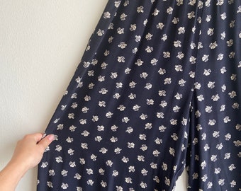 Puede incluir: Pantalones negros de pierna ancha con estampado floral blanco. Los pantalones tienen una cintura elástica.