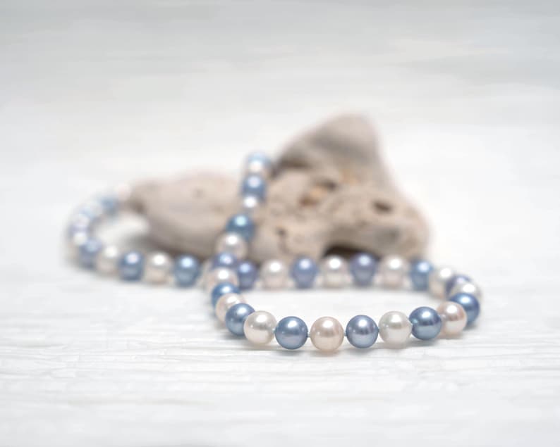 May include: A strand of white and blue pearls on a white background. The pearls are arranged in a circle and are strung on a thin wire.