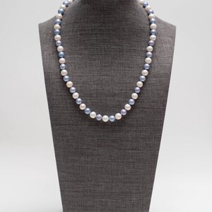 May include: A pearl necklace with white and blue pearls on a gray mannequin.