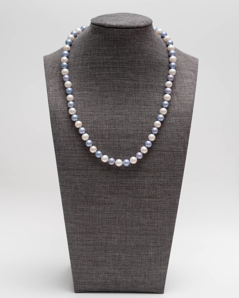 May include: A pearl necklace with white and blue pearls on a gray mannequin.