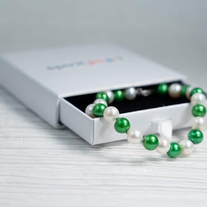 Peut inclure: Une boîte blanche contenant un collier de perles vertes et blanches. Le collier est composé de perles vertes et blanches alternées.