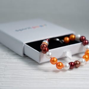 May include: A multi-colored pearl necklace with orange, white, and red pearls in a white gift box.