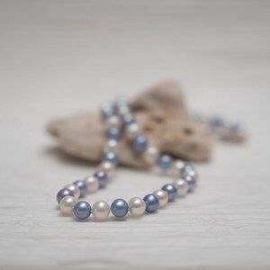 May include: A strand of white and blue pearls draped over a piece of driftwood. The pearls are arranged in a circular pattern, creating a necklace.