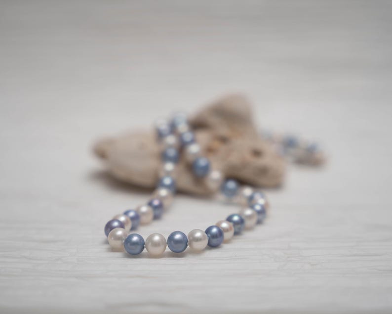 May include: A strand of white and blue pearls draped over a piece of driftwood. The pearls are arranged in a circular pattern, creating a necklace.