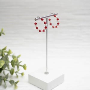 May include: Red and white beaded hoop earrings on a white stand. The earrings are made of small red and white beads.