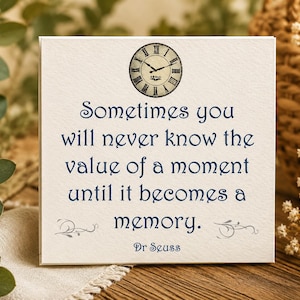 May include: A square white sign featuring a vintage-style clock illustration at the top and the dark blue text: Sometimes you will never know the value of a moment until it becomes a memory. Dr Seuss, with decorative flourishes at the bottom.
