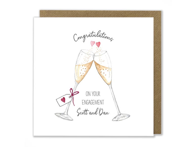 May include: A white card with a watercolor illustration of two champagne flutes clinking. The card says "Congratulations on your engagement Scott and Dan" with two small pink hearts above the flutes.