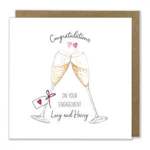 May include: A white card with a brown border. The card has a watercolor illustration of two champagne flutes clinking together. The text on the card reads "Congratulations on your engagement Lucy and Harry".