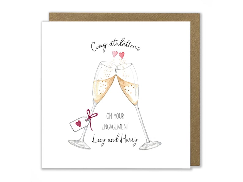 May include: A white card with a brown border. The card has a watercolor illustration of two champagne flutes clinking together. The text on the card reads "Congratulations on your engagement Lucy and Harry".