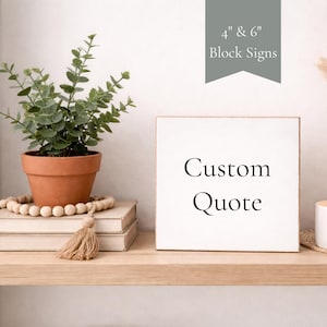 May include: A white square block sign with the words "Custom Quote" in black lettering. The sign is displayed on a wooden shelf with a potted plant, books, and decorative beads. The sign is available in 10 cm and 15 cm sizes.