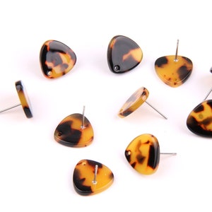 Puede incluir: Un conjunto de diez pendientes triangulares de carey con postes de plata. Los pendientes están esparcidos sobre una superficie blanca.